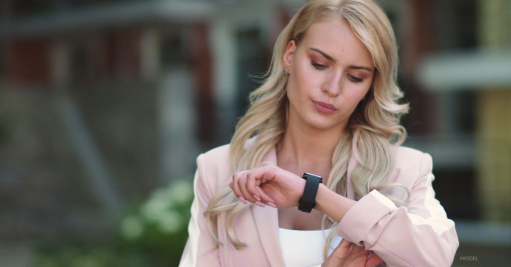 Woman (model) looks down at her watch with a concerned expression.