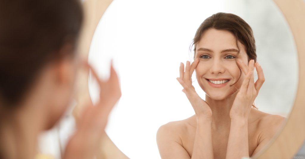 Young woman looking at her face in the mirror (model)